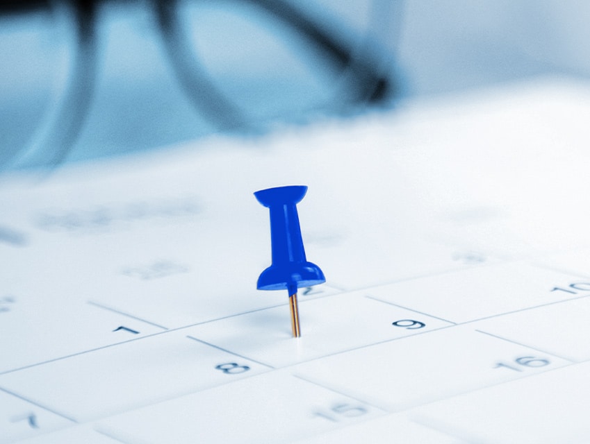 Blauer Reißnagel markiert Datum im Kalender. Terminplanung.